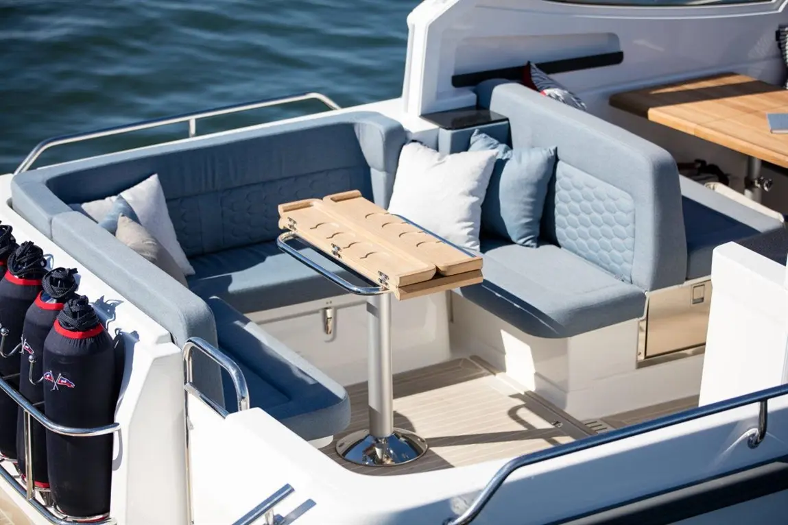 A stylish boat seating area with grey cushions, a modern folding table, and storage for equipment by the water.